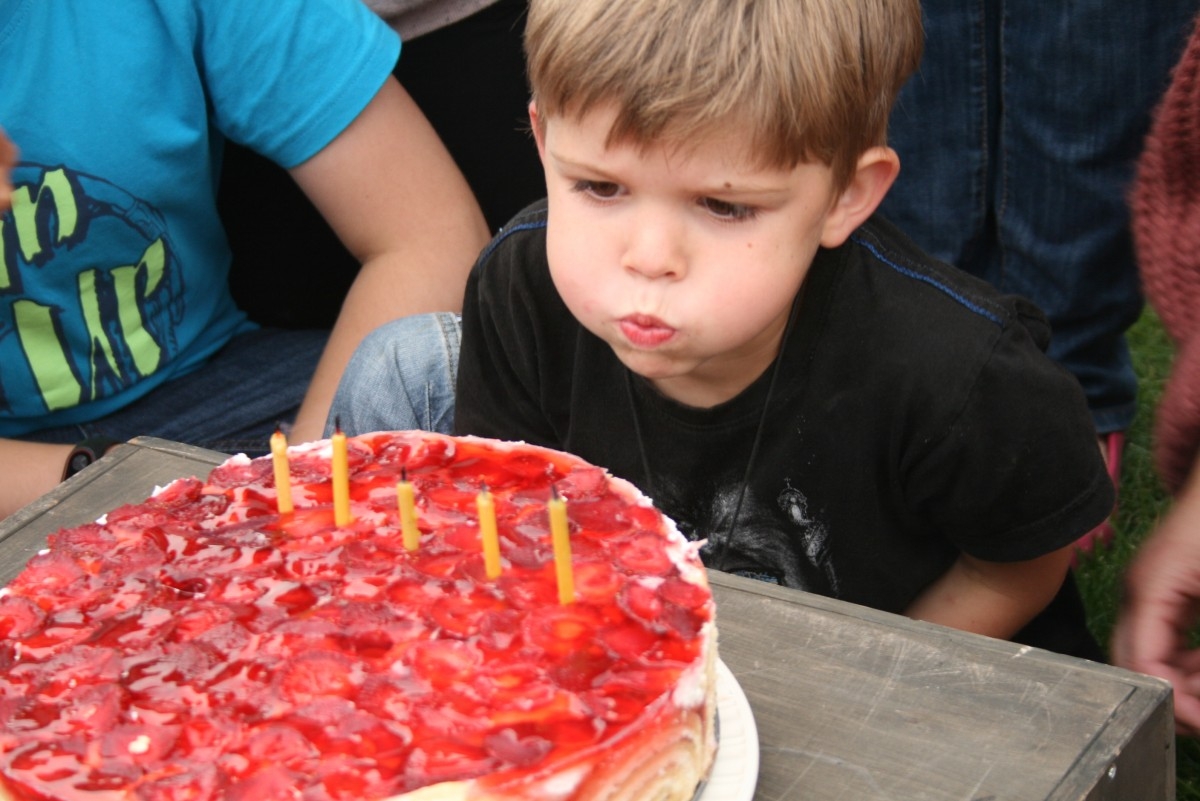 Berniukas pučia žvakutes ant braškinio torto