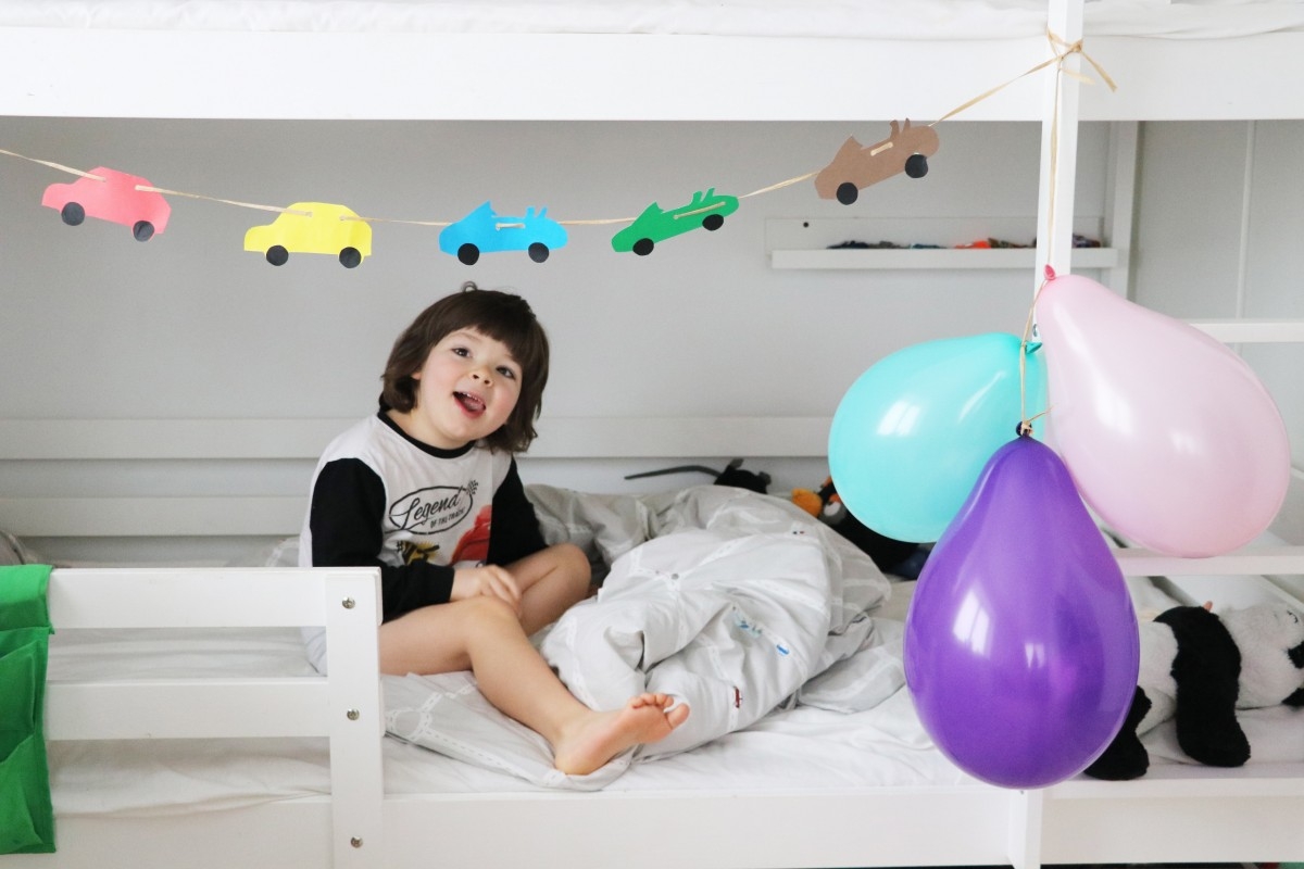 Vaikas žiūri į mašinytes lovoje balionai girlianda
